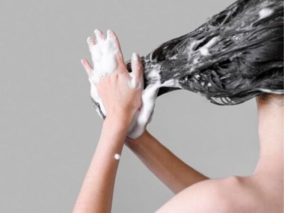 femme brune se lavant les cheveux avec un shampoing et frottant ses longueurs pour faire de la mousse