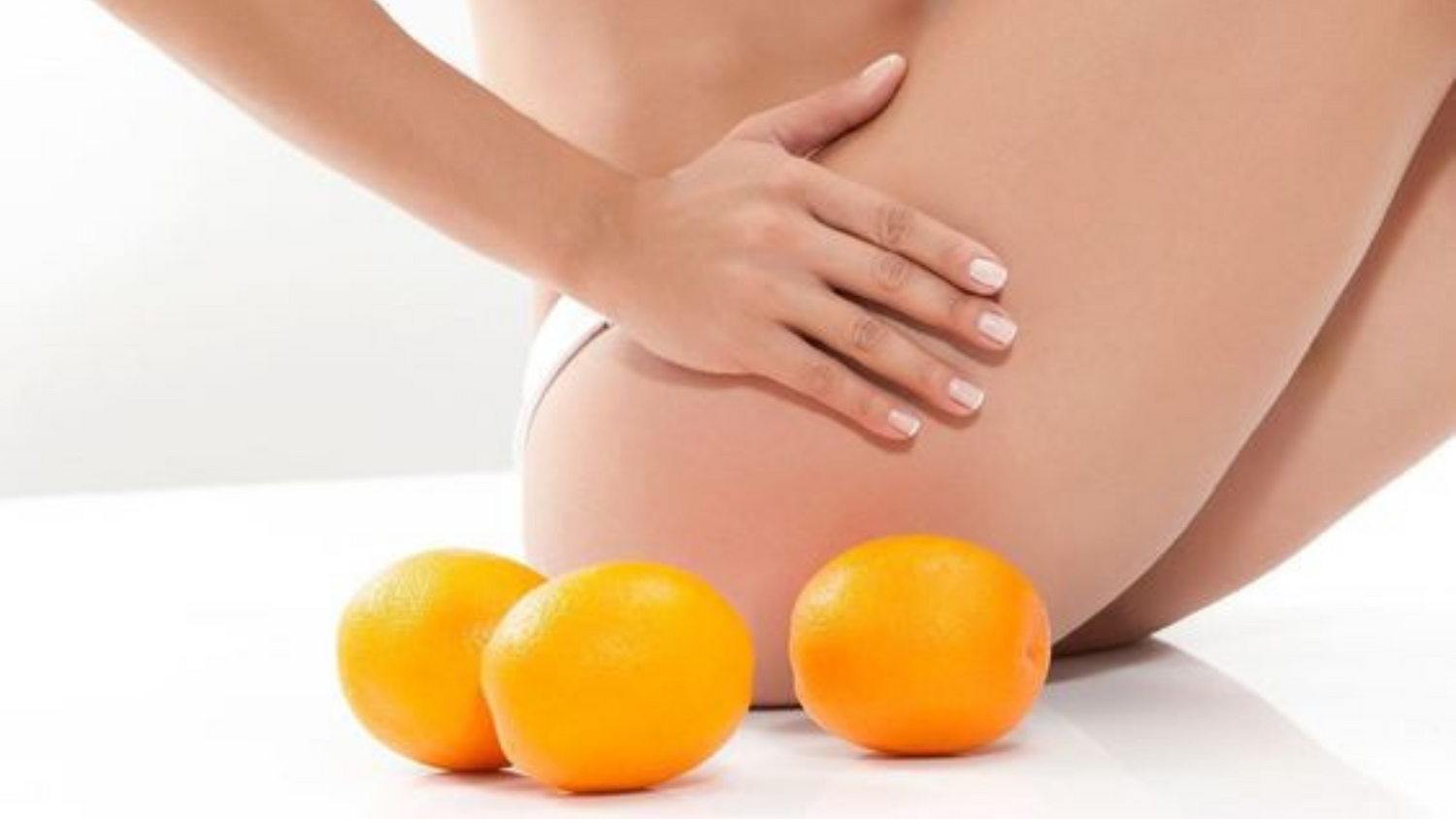 femme se touchant les cuisses assise à côté de 3 oranges, faisant référence à la peau d'orange qui est l'aspect de la peau donné par la cellulite