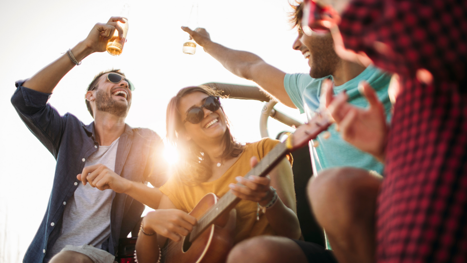 4 amis qui passent un bon moment, réunis l'été, sous le soleil couchant, autour d'une guitare et de verres d'alcool