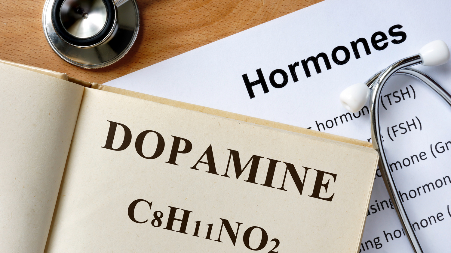 Livre ouvert avec écrit le mot dopamine et dessous le nom de la molécule. Sous le livre une feuille avec écrit "hormones". Posé sur la feuille l'embout du stéthoscope d'un médecin.