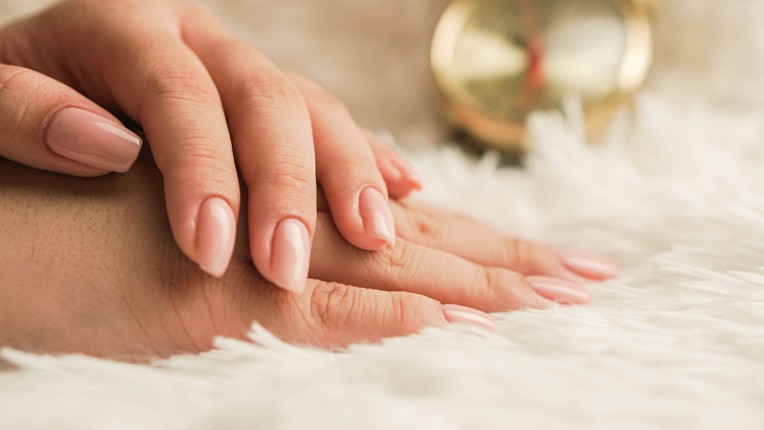 Deux jolies mains posées l'une sur l'autre avec des ongles longs, beaux et forts et brillants décoré d'un vernis nude en guise de mancure.