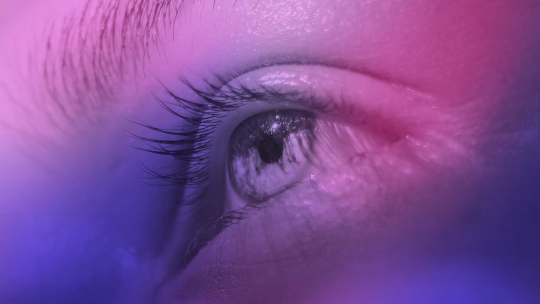 zoom sur un oeil bleu, beau regard surmonté d'un sourcil harmonieux sous des teintes violettes